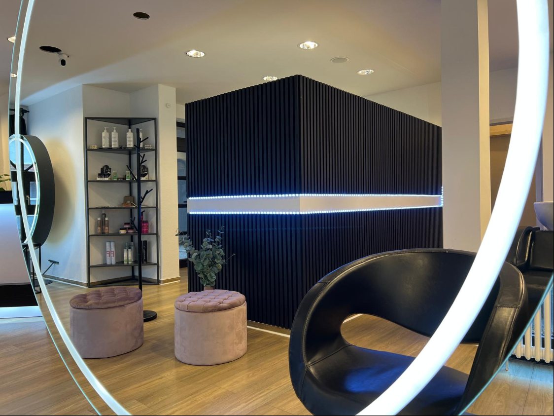Salon mit rosa Hockern, Regal und beleuchteter Wand